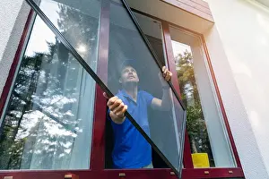 Installing Prints: worker installing mosquito net wire screen on plastic pvc window