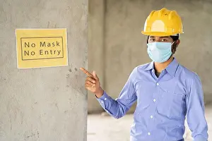 Repairman Prints: worker pointing No Mask No Entry signage notice board on wall at working construction site to protect from coronavirus