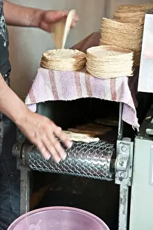 Pulling Prints: worker pulling & stacking tacos from conveyor belt on semi automated mechanized taco making machine Roma district