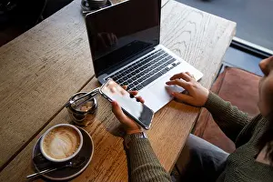 Texting Prints: Working in a coffee shop. Casual looking young woman works on laptop in coffeehouse