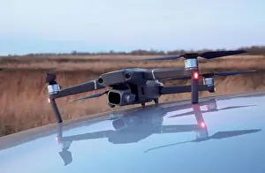 A working drone on the hood of a car and its mirror image in the hood with autumn grass in the background