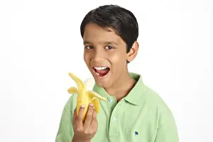Jolly Prints: Ten year old boy showing half peeled yellow banana holding in hand MR#703V