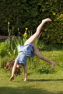 eight year old girl doing cartwheels in school uniform dress after school in garden practicing gymnastics