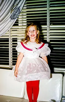 Four year old young girl with blonde hair wearing fancy party dress and red tights standing on a sofa, USA in the 1950s