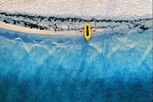 Yellow packraft rubber boat with red padle and turquoise water waves from top view. Beach with yellow sand glowing by sunlight