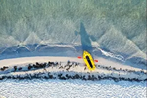 Yellow packraft rubber boat with red padle and turquoise water waves from top view. Beach with yellow sand glowing by sunlight