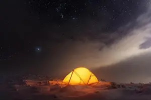 Yellow tent lighted from the inside against the backdrop of glowing city lights and incredible starry sky. Amazing night landscape