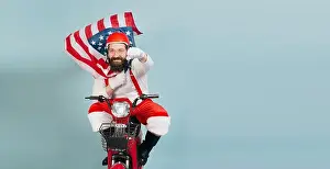 Goggles Prints: Young adult man in a santa costume in a superman pose with a fluttering usa flag in the form of a cape