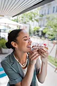 Cafeteria Prints: Young african american woman eating tasty eclair on terrace of sweet shop