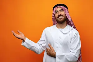 Saudi Arabia Prints: Young Arab man pointing hand to copy space on orange background