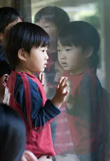 Stare Prints: Young asian boy looking through window with his reflection in the window