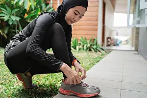 Veil Prints: Young asian muslim women wear sports hijabs and fix shoelaces before jogging