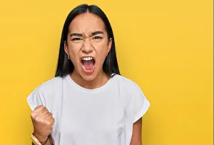 Aggressive Prints: Young asian woman wearing casual white t shirt angry and mad raising fist frustrated