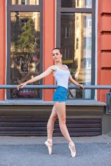 Young ballerina in a white shirt and jeans shorts dancing in pointe shoes on a street