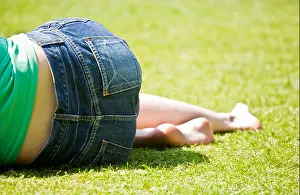 Shoeless Prints: Young barefoot woman wearing denim shorts or skirt lying on grass on a sunny day
