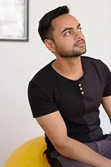 Pensive Prints: Young bearded Indian man thinking while sitting on yoga ball at the gym