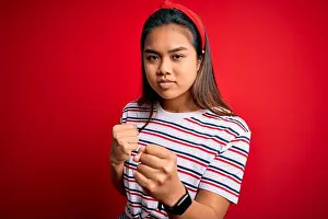 Young Girl Prints: Young beautiful asian girl wearing casual striped t-shirt over isolated red background Ready to fight with fist defense