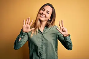 Counting Prints: Young beautiful blonde woman with blue eyes wearing green shirt over yellow background showing