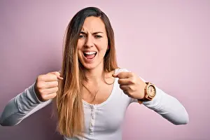 Fist Prints: Young beautiful blonde woman with blue eyes wearing white t-shirt over pink background angry