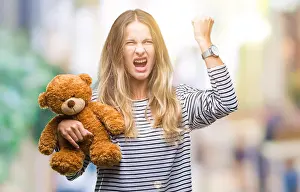 Teddy Prints: Young beautiful blonde woman holding teddy bear plush over isolated background annoyed