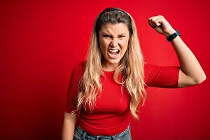 Punching Prints: Young beautiful blonde woman wearing casual t-shirt standing over isolated red background angry