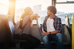 Multicultural Prints: Young beautiful girl is sitting in a bus leaning against the seat of the young handsome man who is turned toward her