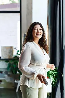 A young beautiful plus size woman stands happily in her stylish office, surrounded by plants