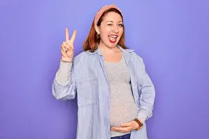 Redhead Prints: Young beautiful redhead pregnant woman expecting baby over isolated purple background smiling with happy face winking