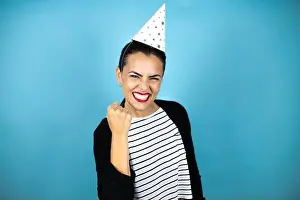 Braids Prints: Young beautiful woman wearing a birthday hat over insolated blue background angry and mad raising fist frustrated