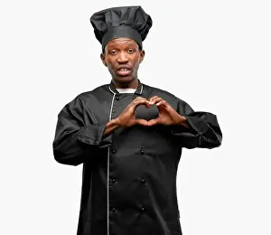 Young black cook wearing chef hat happy showing love with hands in heart shape expressing healthy and marriage symbol