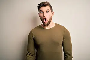 Panic Prints: Young blond man with beard and blue eyes wearing green sweater over white background afraid
