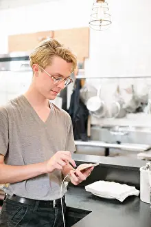 Cell Phone Prints: Young blond man wearing glasses, in a coffee shop, using his cell phone