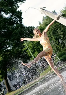 Barefoot Prints: young blond woman in summer dress splashing with water of a fountain, Germany
