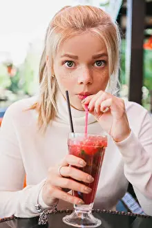 Flirting Prints: young blonde woman with freckles wondering and drinking red coctail with berries and mint in outdoor restaurant