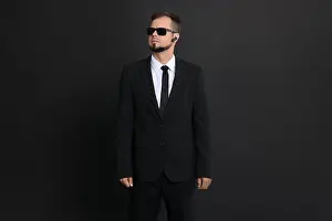Bodyguard Prints: Young bodyguard in suit with sunglasses on black background