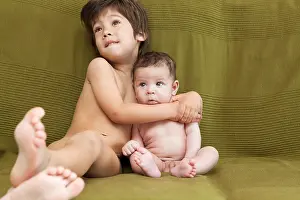 A young boy and his baby brother lying on the couch