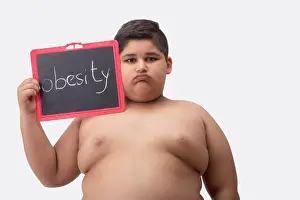 Obese Prints: Young boy bare chested holding a small blackboard with obesity written on it