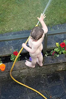 Young boy child bare nude naked in a suburban garden playing with a hose NAOH