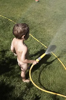 Young boy child playing with a hose in a suburban garden in summer London England UK Naked nude or bare CJWH