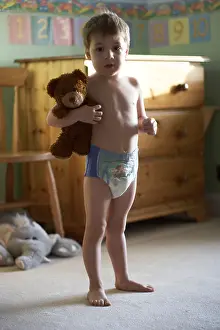 British English Prints: Young boy child standing in his bedroom with teddy bear wearing a pull up nappy CJWH