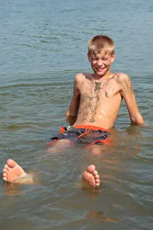 Preteen Prints: young boy covered in mud sitting in a lake