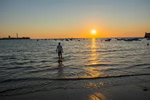 Licking Prints: Young boy licking their feet on the beach at sunset