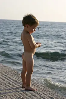 Young boy naked nude or bare playing and standing by the sea in Saronida Greece