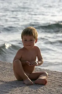 Young boy naked nude or bare sitting by the sea in Saronida Greece