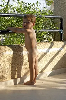 Young boy naked nude or bare standing on a balcony