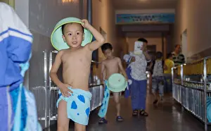 Schoolchildren Prints: A young boy puts a washbasin on his head on his way to take a shower at a boarding school in Taishan