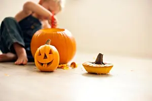 Concentrate Prints: Young boy sitting on the floor uses a tool to hollow out a big pumpkin with a finished small Jack O'Lantern