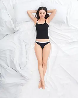 Pajamas Prints: Young brunette woman on bed top view sleeping on back uncovered hands behind head