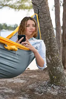 Texting Prints: Young brunette woman hold her mobile phone while relaxing on a hammock