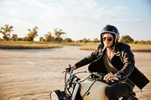 Racer Prints: Young brutal man in a black jacket and glasses driving retro motorcycle